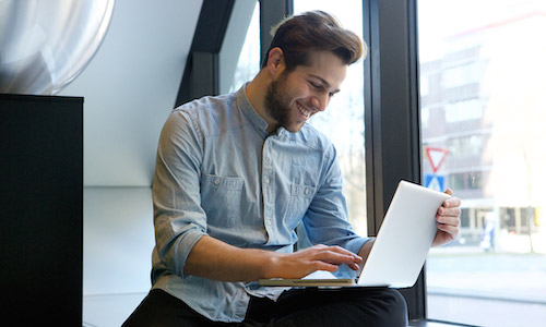 Man sitting by a window, working on a laptop.