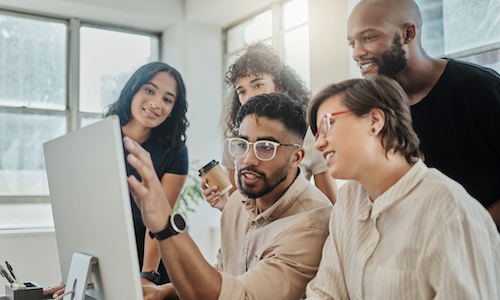 group of people in a work setting clustered around a computer monitor