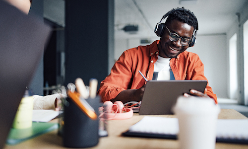 smiling man wearing headphones working on a laptop