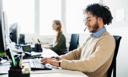 Professionals share a desk and type at their laptops.